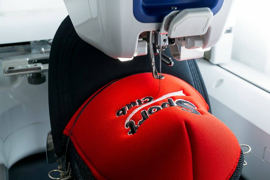 White Embroidery machine and red and black sport cap on the hoop, close up picture